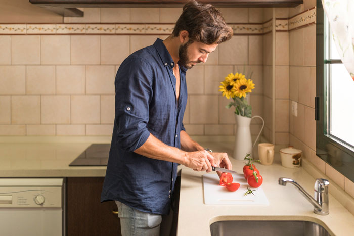 Man showing affection for his sick wife by preparing food in kitchen while sister looks on annoyed.