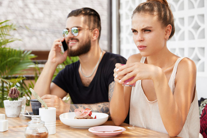 Young woman looks annoyed while her husband talks on phone, highlighting guy's affection for his sick wife tension.