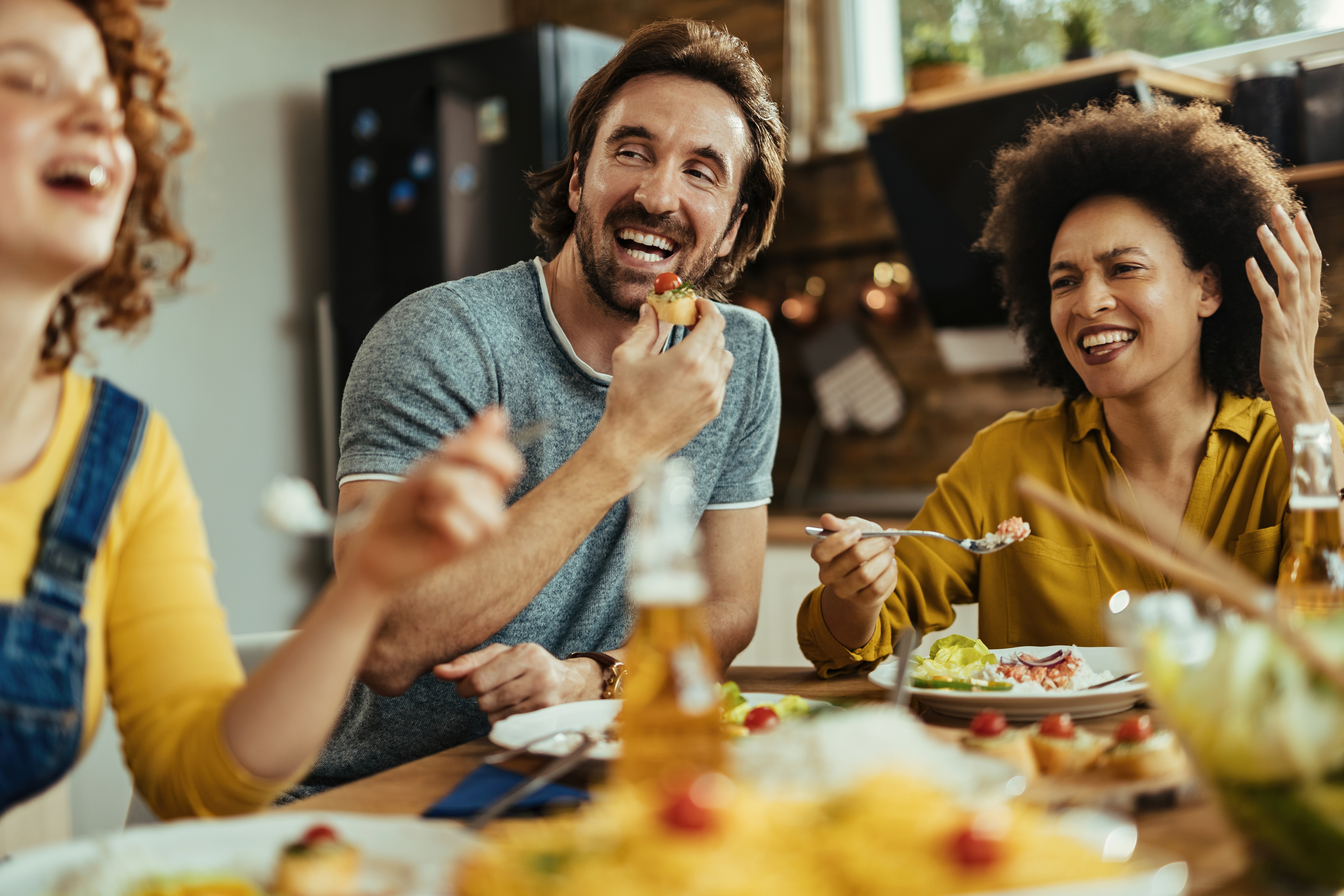 Man and guests enjoying food and drinks at a lively gathering while discussing cooking expectations and reality check.
