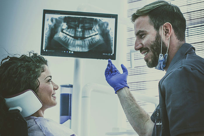 Dentist in blue gloves explaining dental x-ray to smiling patient during a consultation about impactful life lies.