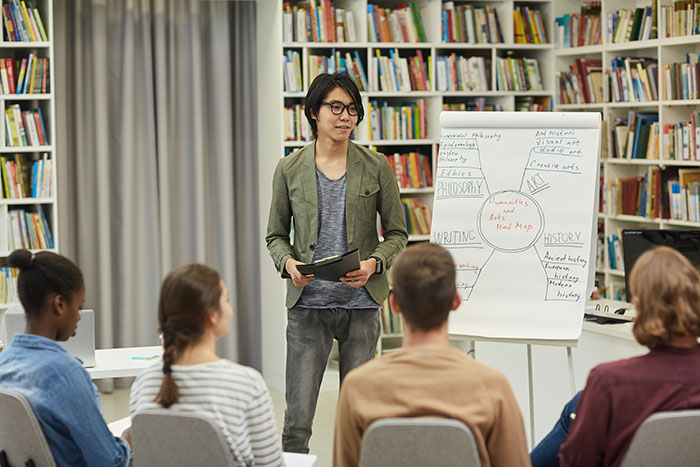 Person presenting to a small group in a library setting, discussing ideas related to lies and their impact on lives.