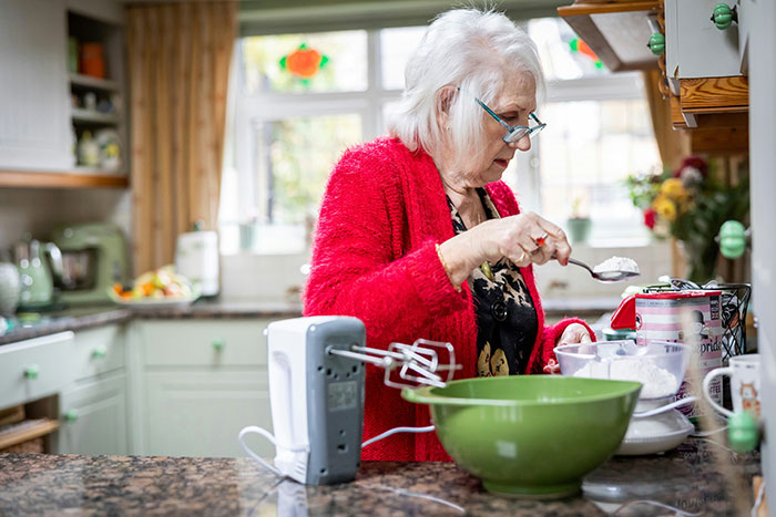 Elderly woman in red sweater preparing food in kitchen, illustrating lies that had a bigger effect on people’s lives.