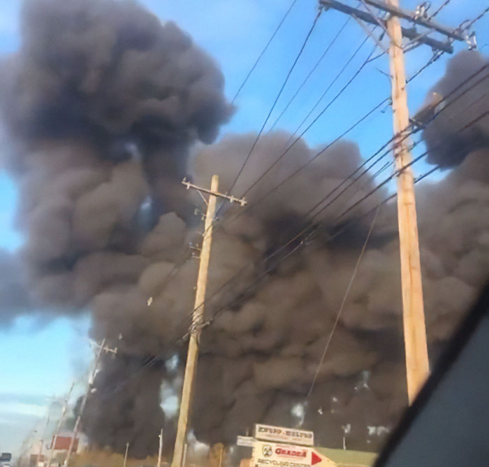 Thick black smoke rising from a UPS plane crash site with multiple casualties visible near power lines.