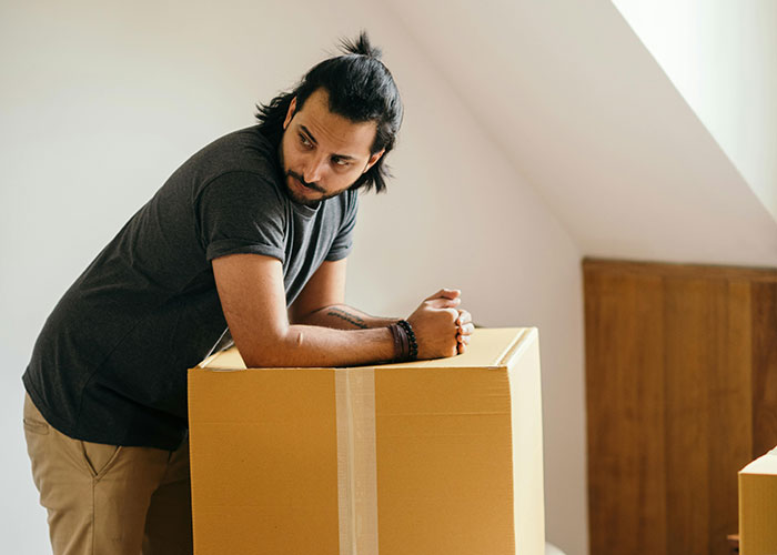 Man leaning on a cardboard box, looking thoughtful, representing a man done with stalkerish HOA president issues.