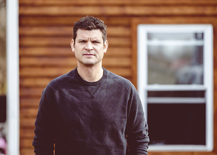 Man standing outside wooden house, looking determined after dealing with stalkerish HOA president and court victory.