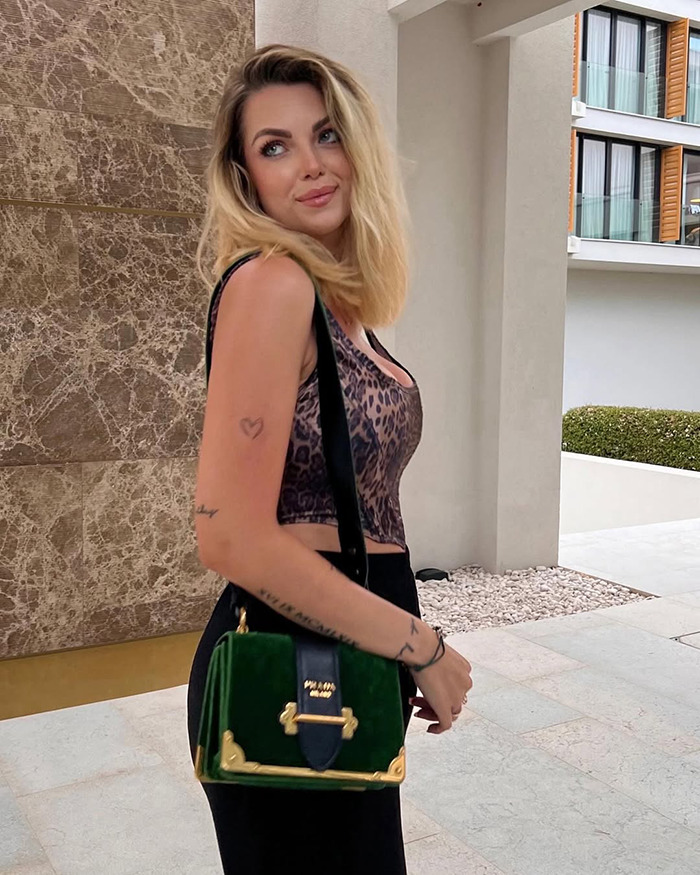 Blonde influencer wearing leopard print top and green handbag, posing outdoors amid mystery surrounding her vanishing after Christmas party.