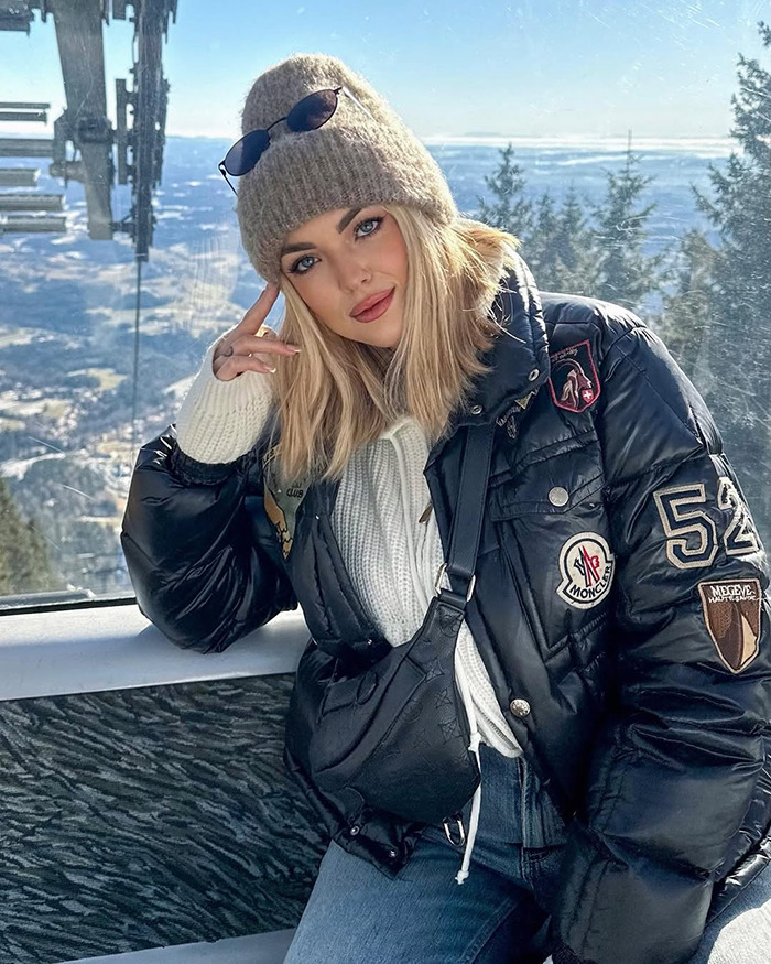 Young influencer wearing winter clothes and a beanie, posing thoughtfully with mountain view, linked to influencer vanishing mystery.