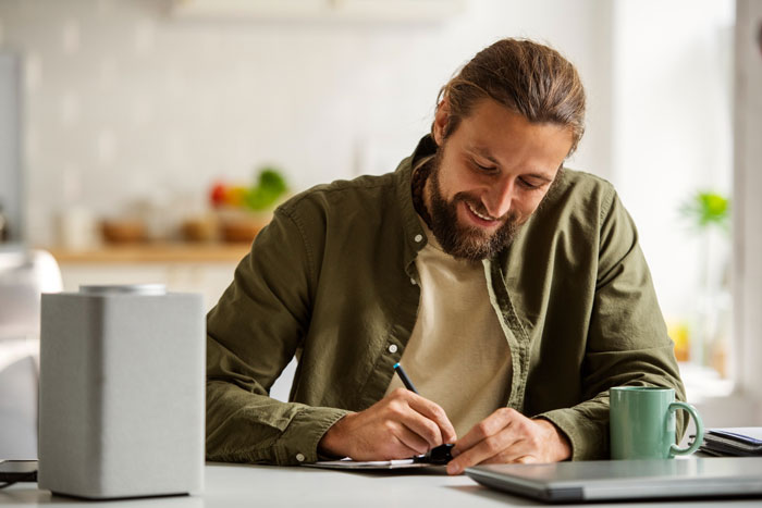 Man with beard writing at desk in bright room, symbolizing stepdad trying to displace kids&rsquo; bio dad from their hearts