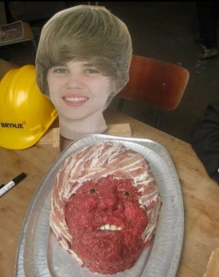Meat sculpture resembling a human face placed on a tray next to a cardboard cutout head, featured in stupid food memes.