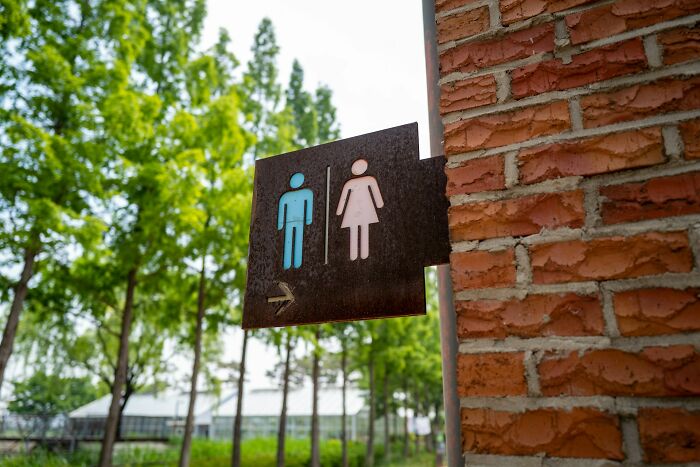 Restroom sign on brick wall outdoors surrounded by trees, illustrating kids doing weird things passed down from parents.