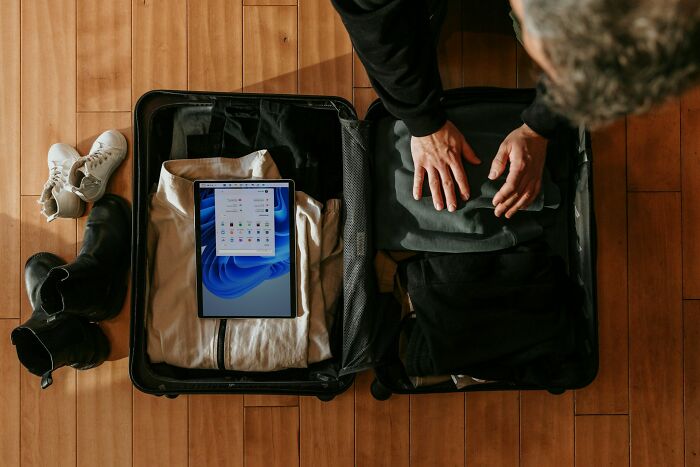 Person packing a suitcase with folded clothes and a tablet, showing kids doing something weird passed down from parents.