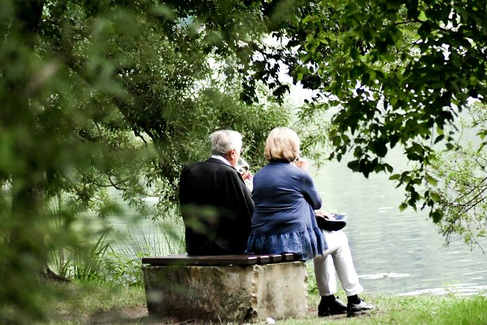 Elderly couple sitting by the lake under trees, reflecting on marriage and the realities of long-term relationships.