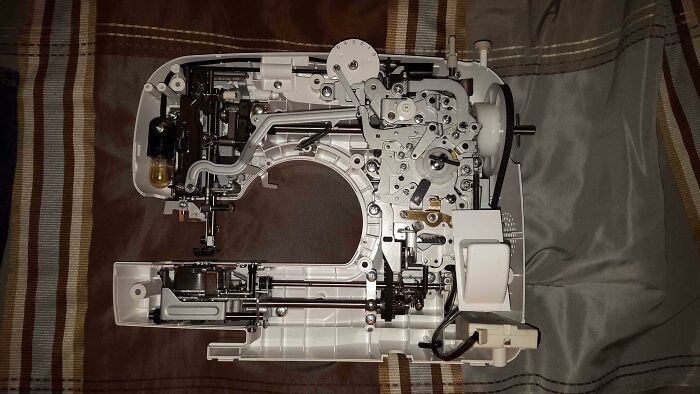 Sewing machine with internal components exposed showing intricate mechanical parts inside the object.