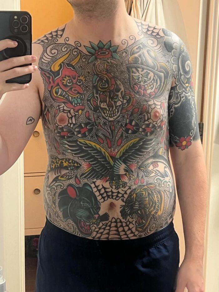 Man showing full chest and arm tattoos in mirror selfie, illustrating tattoo regret and emotional expression.