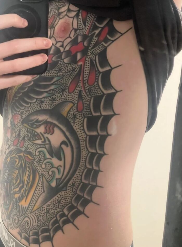Man showing large colorful tattoo on torso with shark, spider web, and other designs, related to tattoo regret and depression.