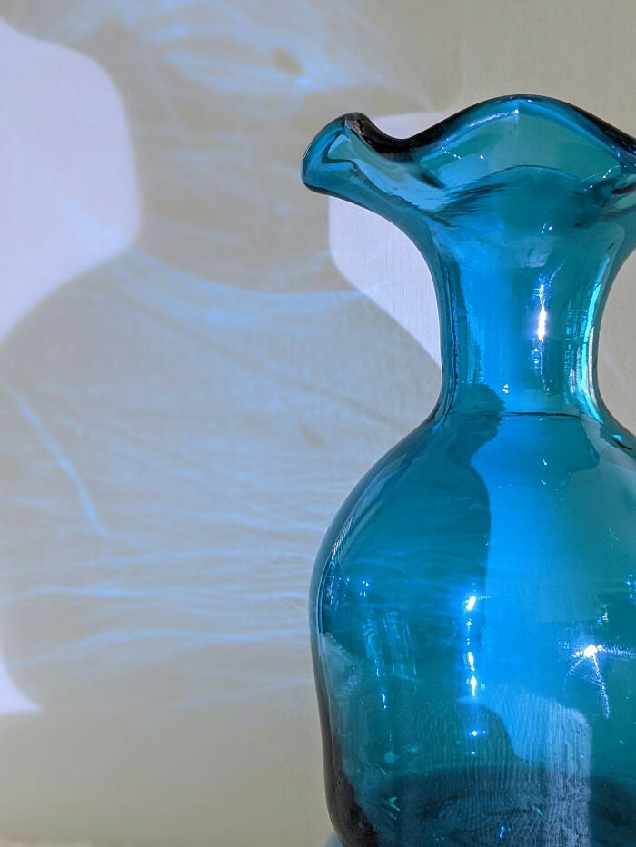 Blue glass vase casting light reflections and shadows, symbolizing eerie finds by garbage men on the job.
