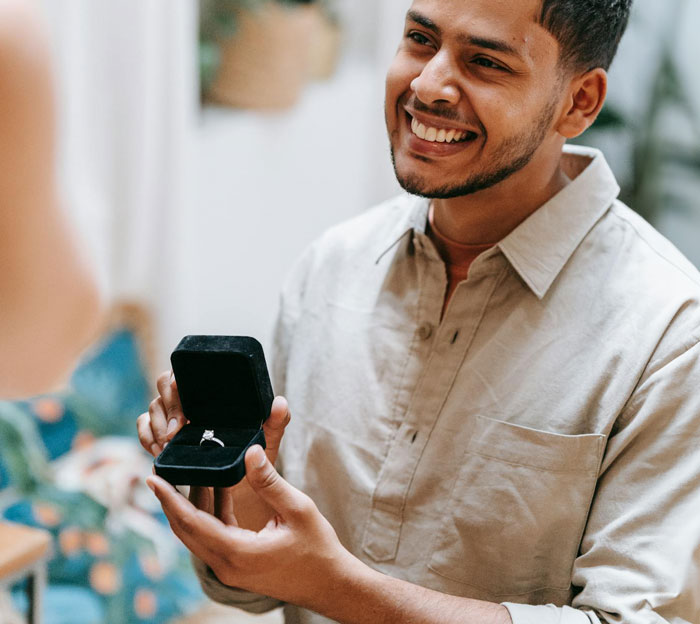 Man smiling and holding an open ring box proposing as a Christmas gift but facing a reality check.