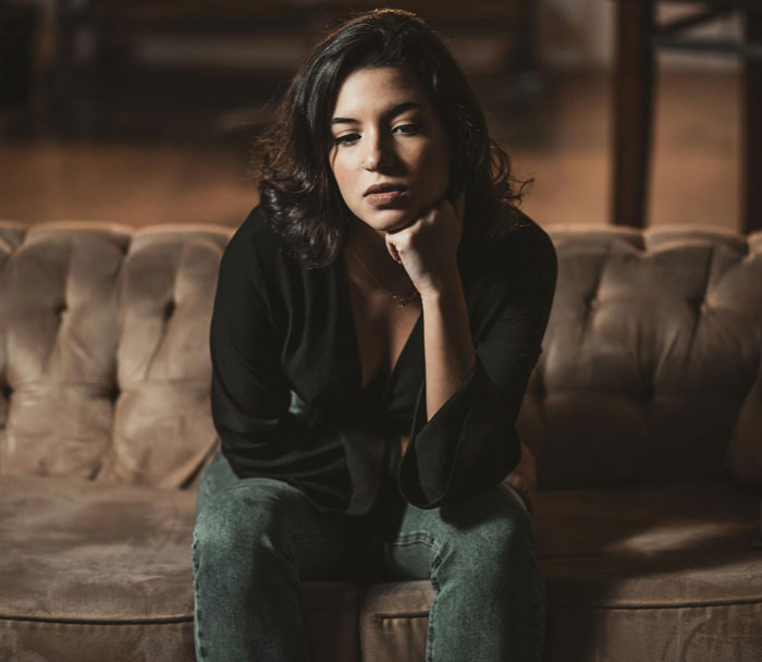 Woman sitting on a couch looking thoughtful and disappointed, representing a man&rsquo;s proposal not counting as a Christmas gift reality check.