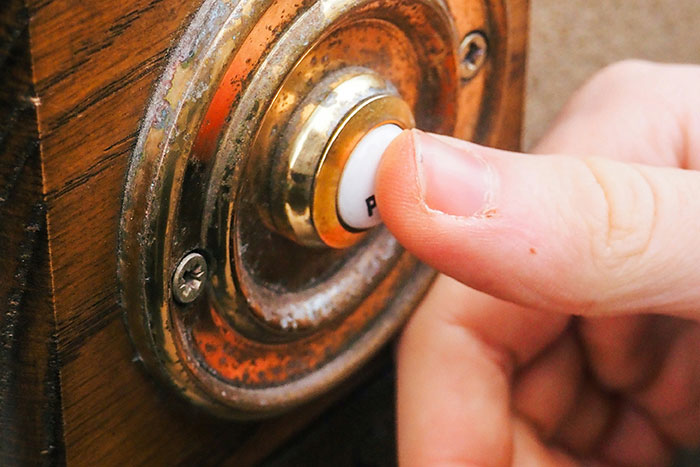 Finger pressing old-fashioned doorbell button representing common Thanksgiving hosting pet peeves and guest annoyances.