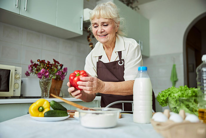 Elderly woman preparing vegetables in kitchen, cooking with Thanksgiving hosting pet peeves in mind.