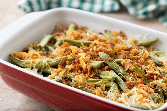 Green bean casserole with crispy fried onions in a red dish, a popular side during Thanksgiving hosting pet peeves.