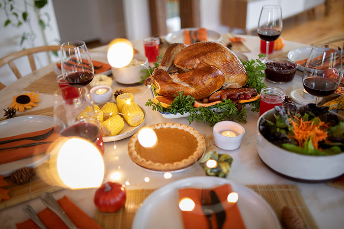 Thanksgiving dinner table set with turkey, pumpkin pie, corn, salad, and glasses of wine highlighting Thanksgiving hosting pet peeves.