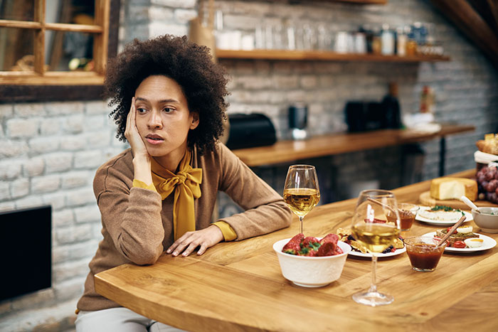 Tired woman sitting alone at Thanksgiving table with food and drinks, showing common hosting pet peeves.