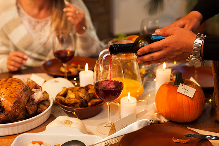 Thanksgiving hosting pet peeves shown with a festive dinner table, wine being poured, and seasonal decorations.