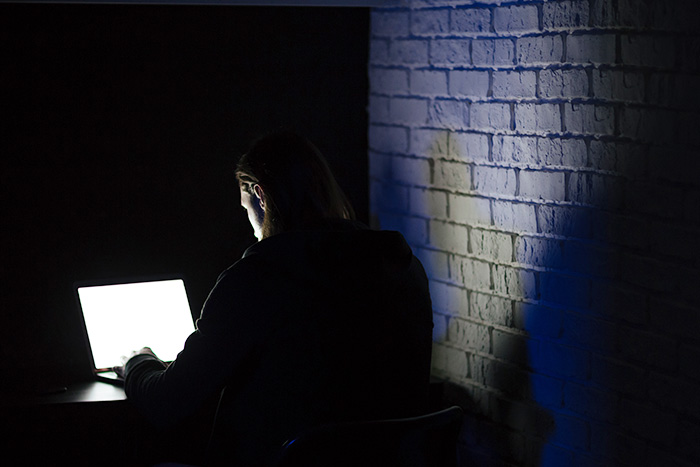 Person in dark room illuminated by laptop light, symbolizing concerns about parents posting children's info online. Person in dark room illuminated by laptop light, symbolizing concerns about parents posting children's info online.
