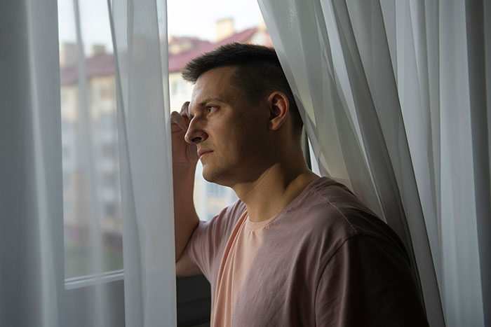 A thoughtful man in a pink shirt looking out a window, reflecting on things men wish they could say anonymously.