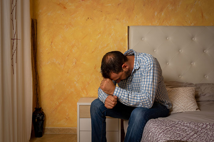 Man sitting on bed with head down in a room, reflecting feelings men wish they could say out loud without judgment.