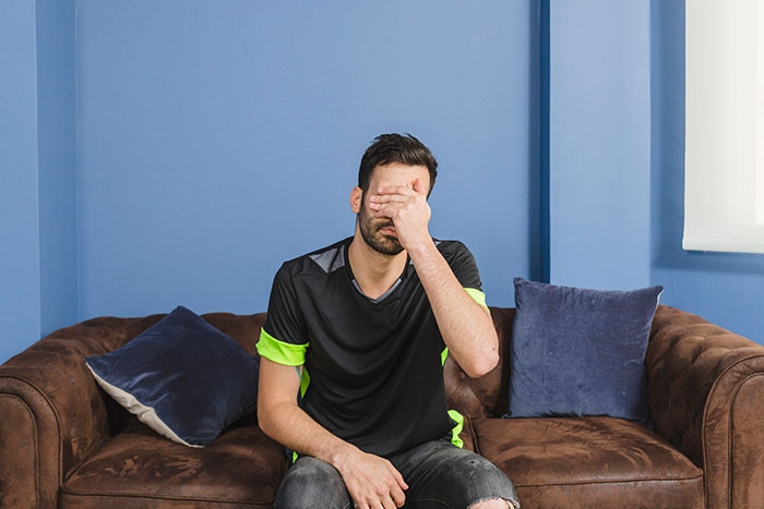 Man sitting on brown couch with hand covering face, expressing emotions men anonymously reveal without being judged.