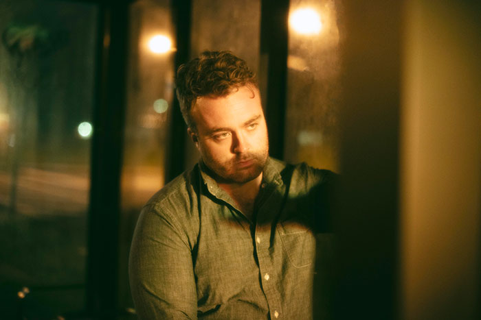 A contemplative man in a green shirt sitting indoors at night, reflecting on anonymous thoughts men wish to share.