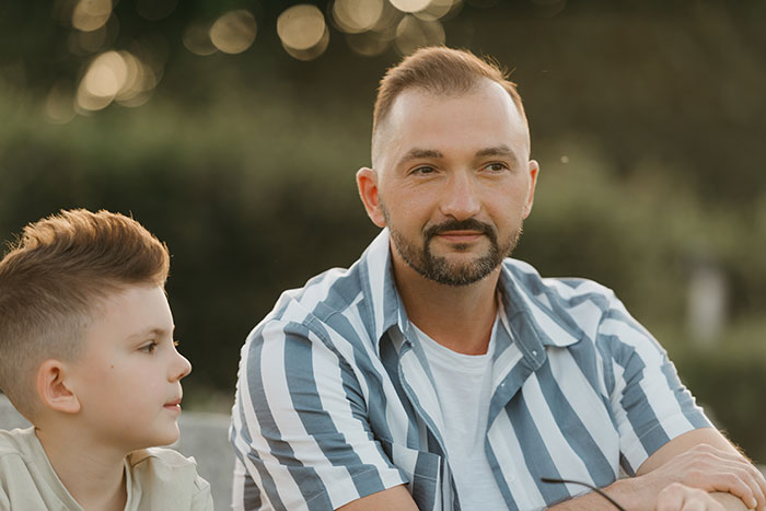 Man with striped shirt and boy sitting outdoors, symbolizing men anonymously revealing thoughts without judgment.