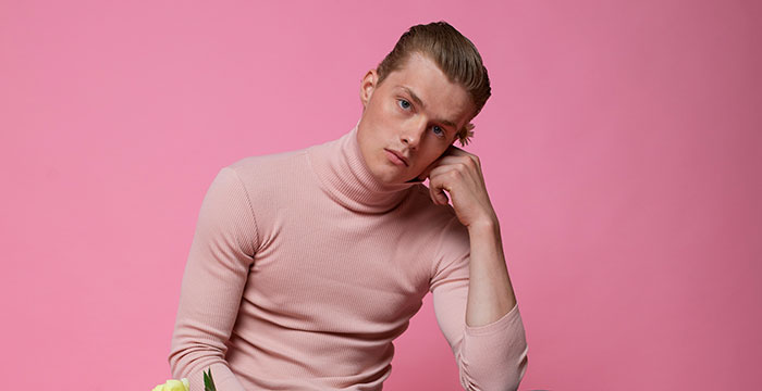 Young man in a pink turtleneck posing thoughtfully against a pink background revealing emotions men wish to express anonymously
