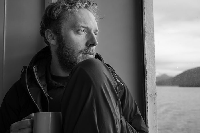 Man looking thoughtfully out a window, holding a mug, representing men anonymously revealing personal thoughts.