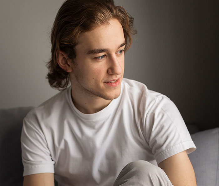 Young man in a white shirt looking away thoughtfully, illustrating men anonymously revealing personal thoughts.