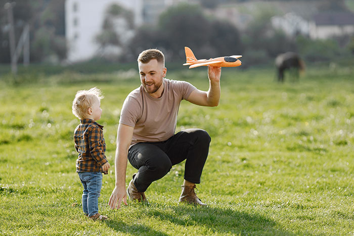 Man playing with a toy airplane with child in a grassy field, capturing moments men wish they could say out loud.