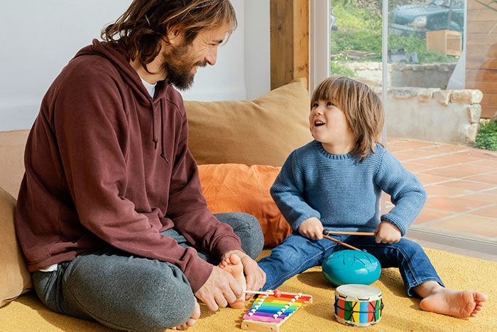 Man and child playing musical instruments together indoors, showing bonding and joyful moments among men anonymously.