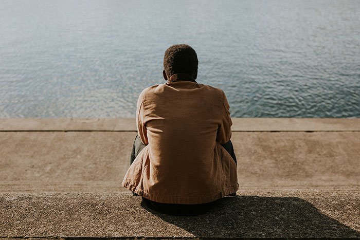Man sitting alone by the water, reflecting quietly outdoors, representing anonymous men revealing personal thoughts.