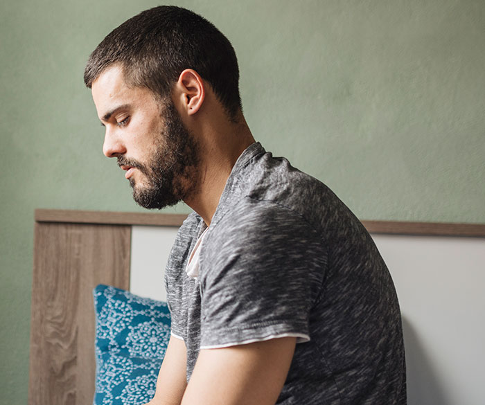 Young man with beard sitting pensively on bed, reflecting on thoughts men wish they could say without judgment.