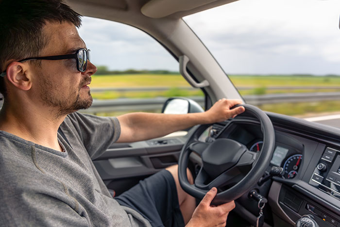 Man wearing sunglasses driving a car on a highway with countryside view, focused on the road ahead.