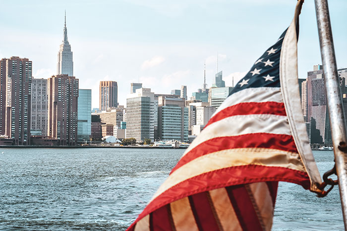 American flag waving with a city skyline in the background symbolizing metal detectors at school in the United States.