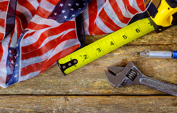 American flag next to a tape measure, wrench, and pen on a wooden table symbolizing metal detectors at school.