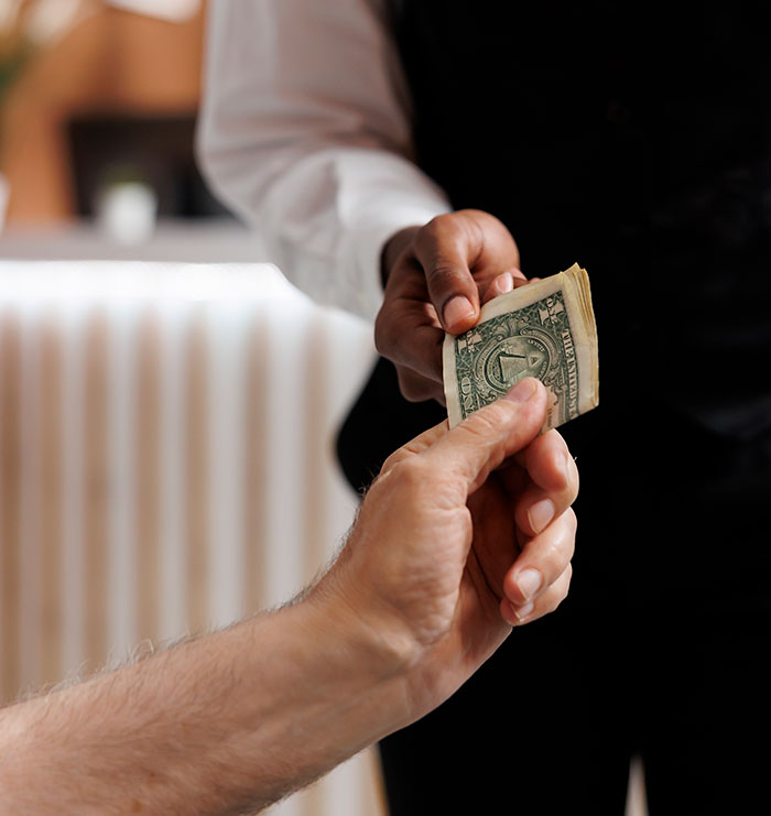 Hand passing US dollar bill in a close-up transaction, illustrating money exchange related to metal detectors at school.