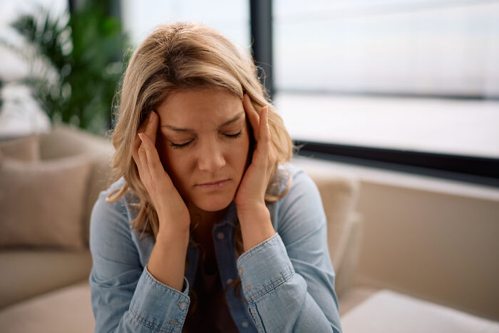 Stressed woman holding her head indoors, reflecting feelings of regret and emotional struggle with having kids.