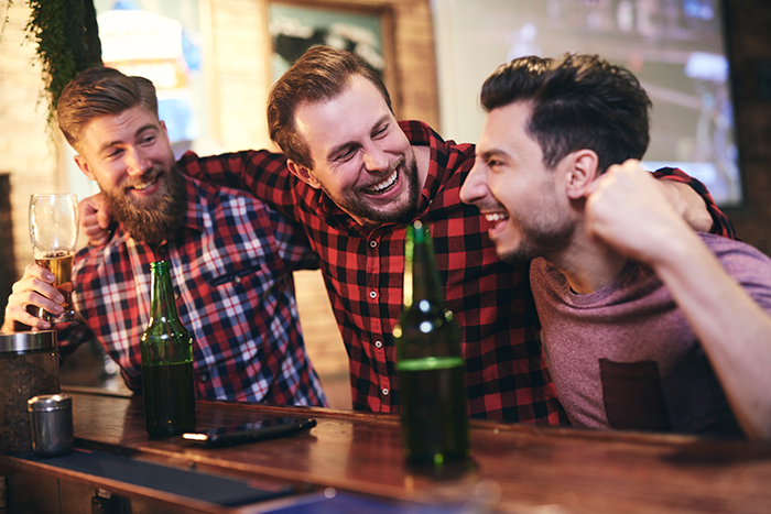 Three men laughing and celebrating at a bar, with a man happy after his ex-wife was caught cheating.