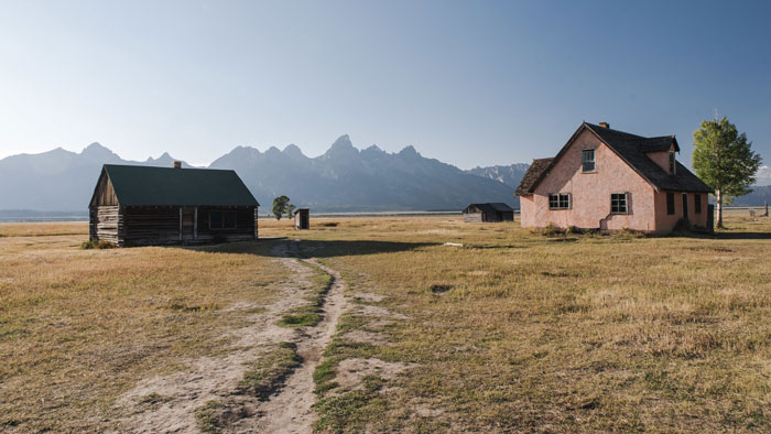 Rural landscape with old farmhouse and barn near mountains, reflecting an inherited tractor dispute involving toxic MIL and son-in-law.