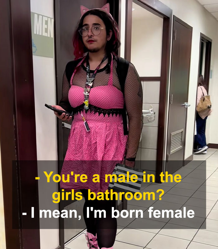 Bearded trans man wearing pink dress and cat ears standing near restroom door, sparking debate over women's restroom use.