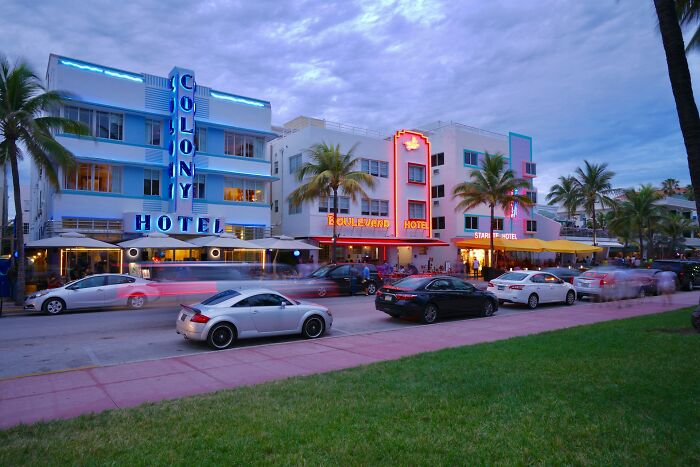 Miami street scene at dusk with neon-lit hotels, palm trees, and cars along the iconic Ocean Drive.